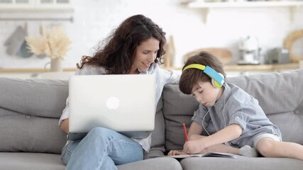 Wall Mural - Loving mom looking at small son drawing in notebook while working from home. Happy businesswoman or freelancer female enjoy remote business occupation on lockdown spend more time with preschool child