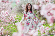 © dmitriisimakov - Beautiful woman in a dress with flowers walks through the flowering garden in spring