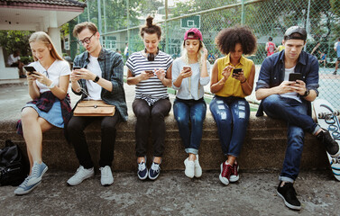 Wall Mural - Young adult friends using smartphones together outdoors youth culture concept