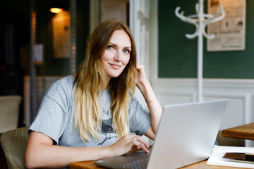 Portrait of young woman using technology of smartphone and looking at laptop. Young woman freelancer using laptop computer working in restaurant or hipster indoor cafe with coffee. Home office concept