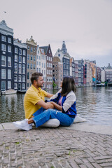 Wall Mural - Amsterdam Netherlands, happy couple man and woman on a summer evening at the canals of Amsterdam. Man and woman mid age Asian girl and European men on city trip in Amsterdam Netherlands