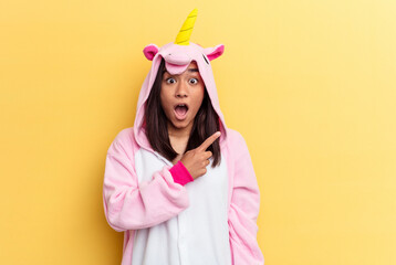 Wall Mural - Young mixed race woman wearing a unicorn pajama isolated on yellow background pointing to the side