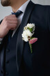 Groom in a dark blue suit with a boutonniere adjusts his tie looking to the side in close-up