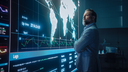 Senior Computer Science Engineer Looking at Big Screen Display Showing Global Map with Data Points. Telecommunications Technology Company System Control and Monitoring Room with Servers.