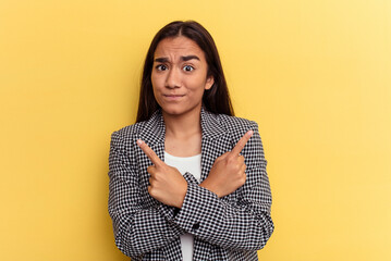 Wall Mural - Young mixed race woman isolated on yellow background points sideways, is trying to choose between two options.