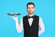 Attractive young waiter holding empty silver tray over blue background