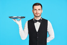 Attractive Young Waiter Holding Empty Silver Tray Over Blue Background