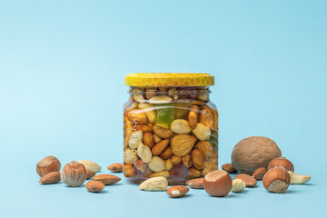 Wall Mural - A glass jar with honey and nuts and scattered nuts on a blue background.