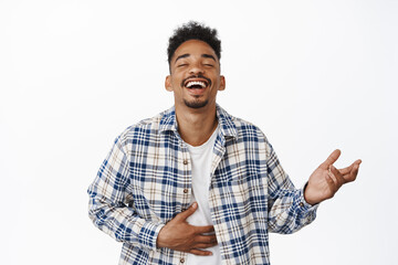 Happy african american guy laughing out loud, watching smth funny, chuckle with hand on belly and closed eyes, siling, having fun, standing against white background