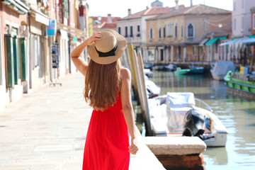 Wall Mural - Beautiful slim model with red dress and hat walking in Murano, Venice