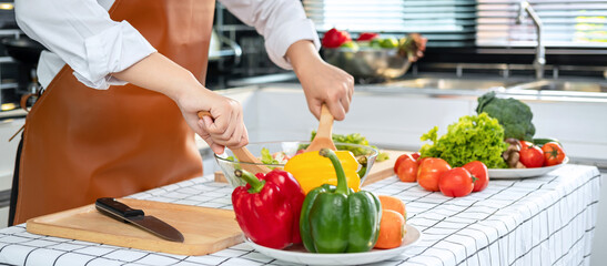 Poster - Asian housewife wearing apron and using ladle to mixing vegetable salad in bowl while standing preparing