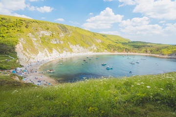 Wall Mural - Tourists and boats enjoy the beach and bay at the colourful seaside Lulworth Cove on a sunny summer day in Dorset, England, UK.