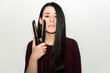 © AliciaFdez - Pretty young woman with dark long hair holding a flat iron in one hand. Hair straightener