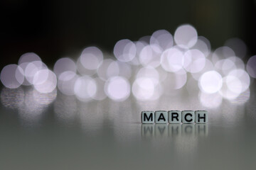 MARCH is a word written on a white block. MARCH is the word for your design, concept. Beautiful bokeh in the background