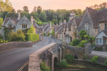 The charming, quaint, historic, medieval Cotswolds English village of Castle Combe in Wiltshire, UK along the By Brook river during a quiet golden sunset or sunrise.