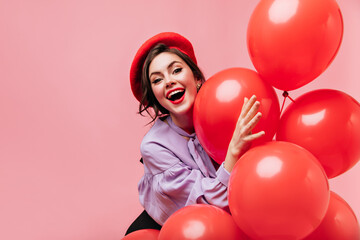 Poster - Naughty woman in red beret is laughing and having fun on pink background with large balloons