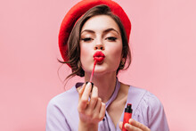 Portrait Of Young Girl In Red Beret Painting Her Lips With Bright Lipstick On Pink Background