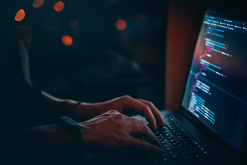 Wall Mural - the code is on a laptop on a wooden table in front of the window in the dark with a view of the ligh