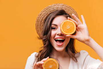 Wall Mural - Optimistic woman in straw hat covers her eyes with orange and smiles while looking at camera