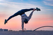 Silhouette of flexible female circus artist doing handstand on the dramatic sunset and cityscape. Concept of individuality, creativity and outstanding