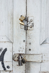 Close up of white wooden door closed with four padlocks.