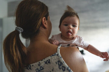 Wall Mural - adult woman mother holding her three months old baby daughter while standing in room at home - growing up motherhood and parenting concept