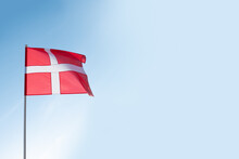 Danish flag waving in wind. Flag of Denmark on blue sky background. Empty copy space.