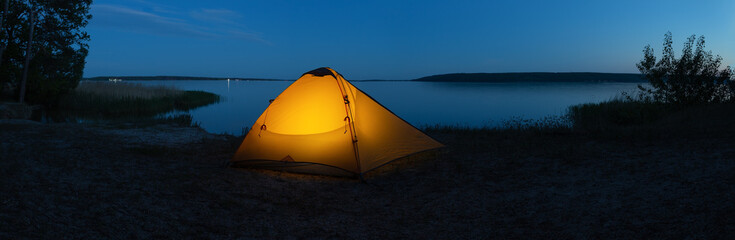Wall Mural - orange illuminated tourist tent on lake in evening