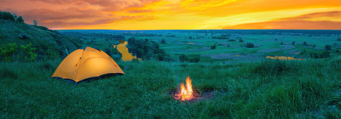 Wall Mural - orange tourist tent on hill above river under orange dramatic sky