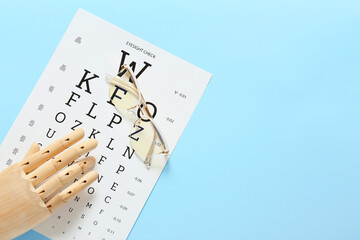 Eyeglasses with wooden hand and eye test chart on color background