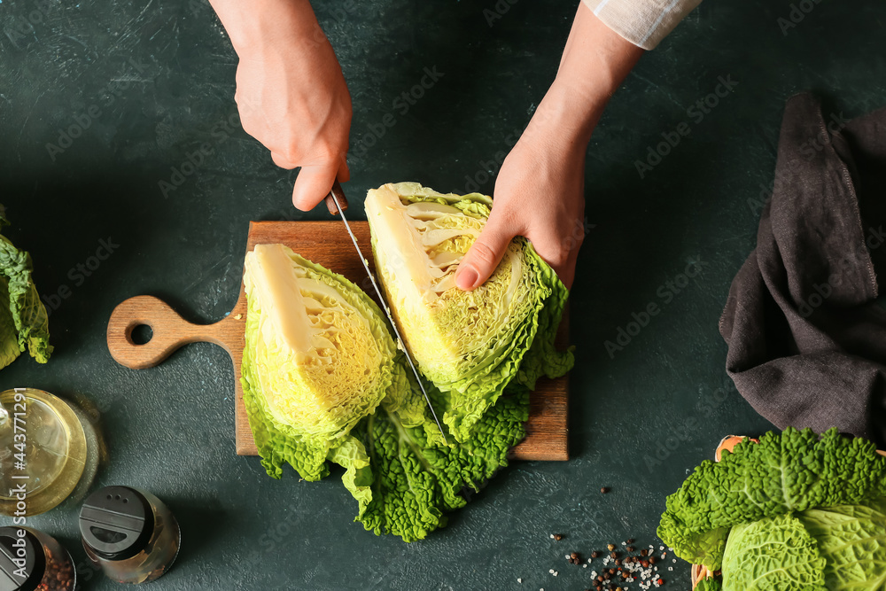Woman cutting fresh savoy cabbage on table