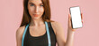 © Daria Lukoiko - Fitness girl smiling and holding a phone with a mockup and posing hold measure tape in black sportswear on a pink background. Slim woman with a beautiful athletic body and tanned skin
