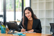 © amnaj - Beautiful Asian businesswoman work by taking notes with tablet at office. Looking at camera.