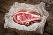 matured raw rib-eye steak in paper on wooden background