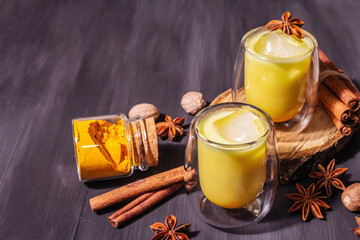 Golden turmeric milk with ice on black wooden background