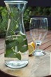 Glass, lemon and bottle filled with water and lemon balm, standing on a round wooden tray on wooden table outside.  
