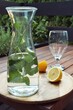 Glass, lemon and bottle filled with water and lemon balm. Standing on a round wooden tray on wooden table outside. 