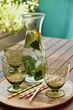 Glasses and bottle filled with water and lemon balm. Standing on a round wooden tray on wooden table outside. Top view at angle. 