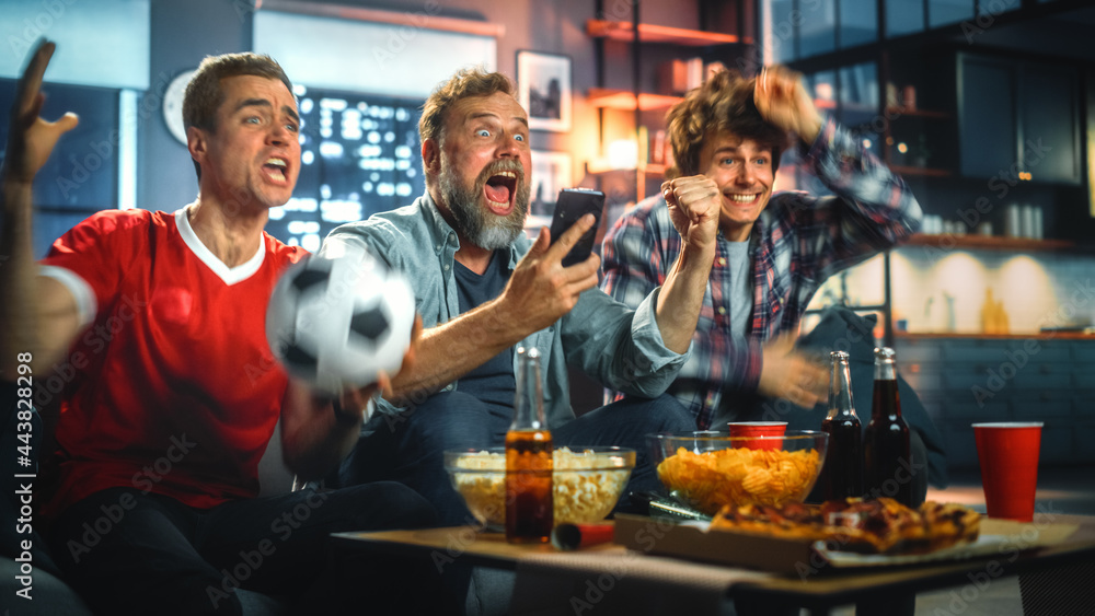 Night at Home: Three Soccer Fans Sitting on a Couch Watch Game on TV, Use Smartphone App to Online Bet, Celebrate Victory when Sports Team Wins. Friends Cheer Eat Snacks, Watch Football Play. - obrazy, fototapety, plakaty 