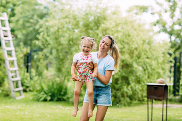 A young mother and her cute little girl are having fun in a sunny garden. The concept of a happy childhood and motherhood, a mother holds her little daughter in her arms