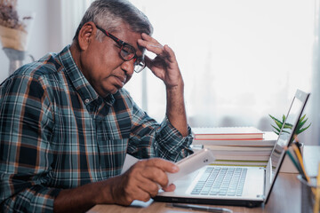 Senior man seriously working with laptop computer at home.