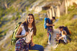 © Studio Romantic - Smiling woman hiker with backpack looking at camera with group of friends hikers resting at background on nature