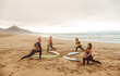 © merla - Group of people stretching at the beach, before starting a surf session