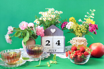 Wall Mural - Calendar for July 24 : the name of the month of July in English, cubes with the number 24, bouquets of wild flowers, jam, fruit, cups of tea, white napkins, green background