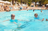 Fototapeta Na ścianę - Two elderly senior women with grey hair, wearing blue swimsuit resting and swimming on their backs in hotel pool