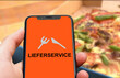 © keBu.Medien - Person hält Smartphone mit einer Lieferservice App vor einer Pizza im Karton, Lieferdienst, Lieferservice, Essen, Gastronomie