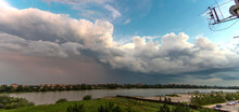 Powerful Thunderstorm Front With Dark Clouds And Blue Sky Over A Flat River - Panorama On A Summer Day