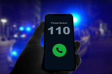 Person Hält Smartphone In Der Hand Und Ruft Den Notruf 110 Der Polizei, Im Hintergrund Des Blaulicht Von Polizeiautos Bei Nacht
