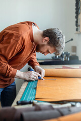 Male tanner making cutting scheme of bag working at leather workshop. Handcrafted creating