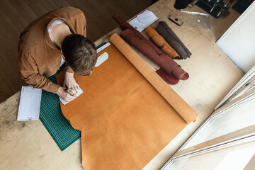 Male tanner making cutting scheme of bag working at leather workshop. Handcrafted creating